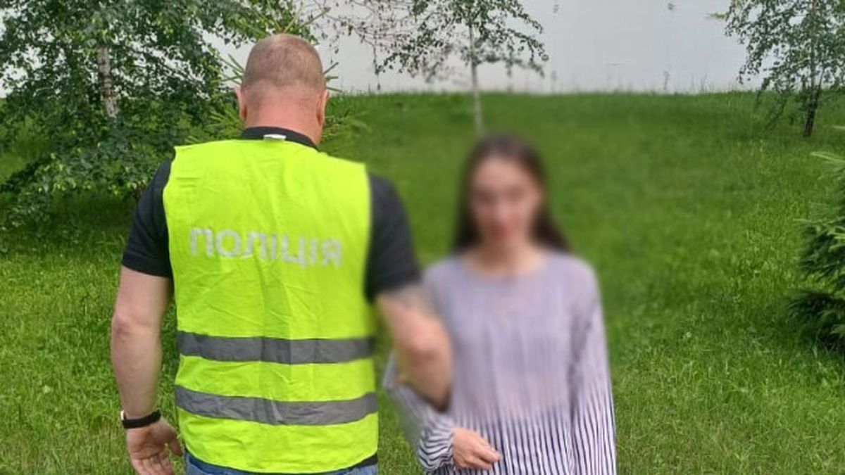 У Києві судитимуть 28-річну жінку, яка розсилала наркотики поштою по всій Україні Молода жінка перебуває поруч із поліціянтом у зеленій жилетці в парку Києва, можливо, під час затримання або розслідування. На тлі — зелені дерева та трава, навколо спостерігається природне середовище. Обличчя жінки розмито для збереження приватності.