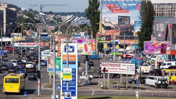 У Києві псевдопоштарка «обміняла» пенсіонерці 267 тисяч гривень на папірці Багатолюдна транспортна розв'язка з автомобілями, рекламними щитами і вуличним освітленням у Києві, фото сучасного міського руху.