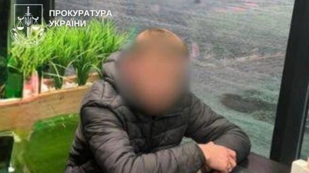 У Києві судитимуть жінку за погрозу підірвати управління поліції Підозрюваний у темній куртці із заблюреним обличчям сидить за столом, на фото водяний знак Прокуратури України