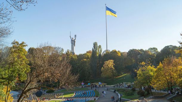 Тепло, оповіщення, зарядки: головне в Києві за тиждень Осінній парк із прогулянковими алеями, монумент Батьківщина-Мати та великий прапор України на тлі блакитного неба в Києві