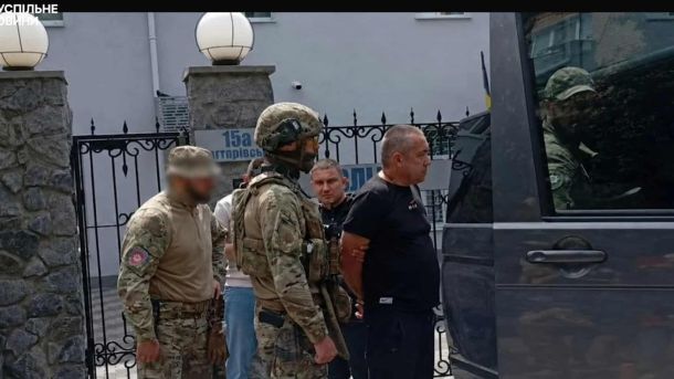 Атака на Київ: у Голосіївському районі горіли склади за двома адресами Правоохоронці у формі ведуть затриманого Станіслава Лучанова до мікроавтобуса — кадр із відео Суспільне Новини
