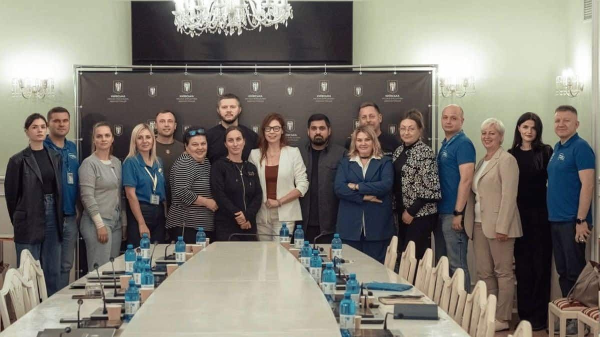 КМВА підписала меморандуми з волонтерами: разом допомагатимуть киянам Група людей стоїть у залі для нарад перед довгим столом на фоні банера Київської міської адміністрації