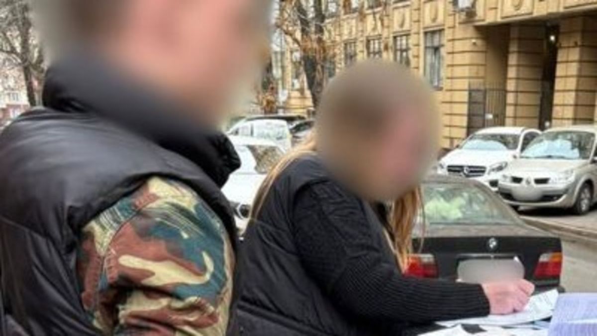 Нотаріусу на Печерську оголосили підозру за схему із землею Підозрювана підписує документ. Поряд правоохоронець