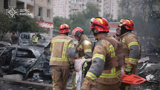 Атака на Київщину: 6 загиблих, 23 постраждалих Четверо рятувальників ДСНС несуть постраждалого на ношах повз згорілий автомобіль