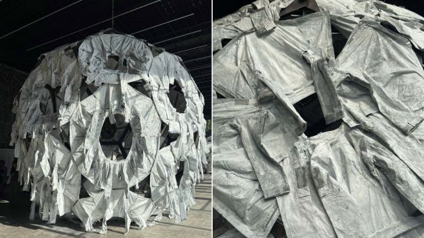 У Києві поліцейські затримали хулігана, який зламав світильник у метро — йому світить до 5 років Велика інсталяція у вигляді кулі, складеної з численних сірих захисних костюмів або комбінезонів, підвішена в просторому залі