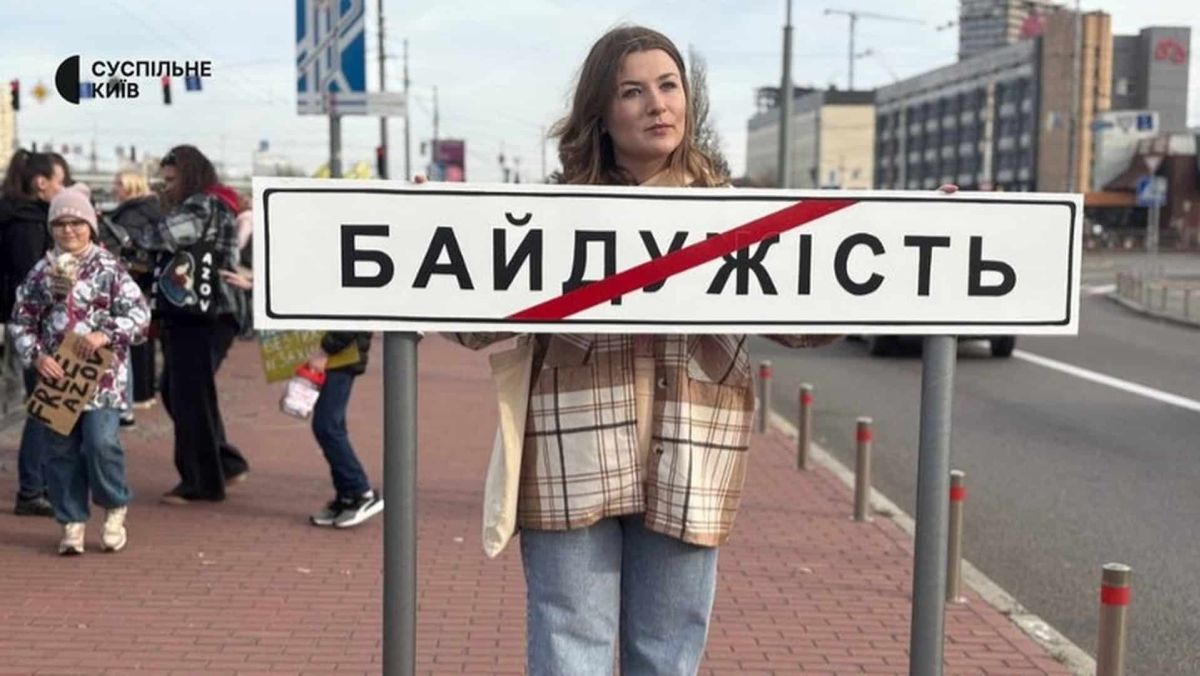Біля метро «Почайна» в Києві пройшла акція рідних, які чекають на повернення своїх близьких Жінка тримає дорожній знак з написом "БАЙДУЖІСТЬ", перекреслений червоною смугою