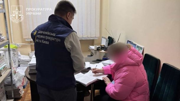 У Києві на військового напали з ножем: затримали двох Правоохоронець стоїть біля жінки в рожевій куртці яка за столом підписує папери