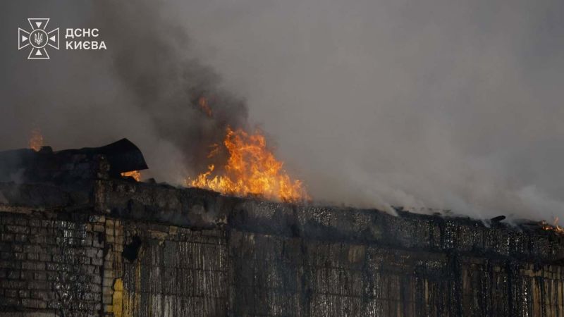 Головні новини Києва | Kyiv.News Дах пошкодженої будівлі охоплений полум'ям і густим димом удень після нічної пожежі в Києві.