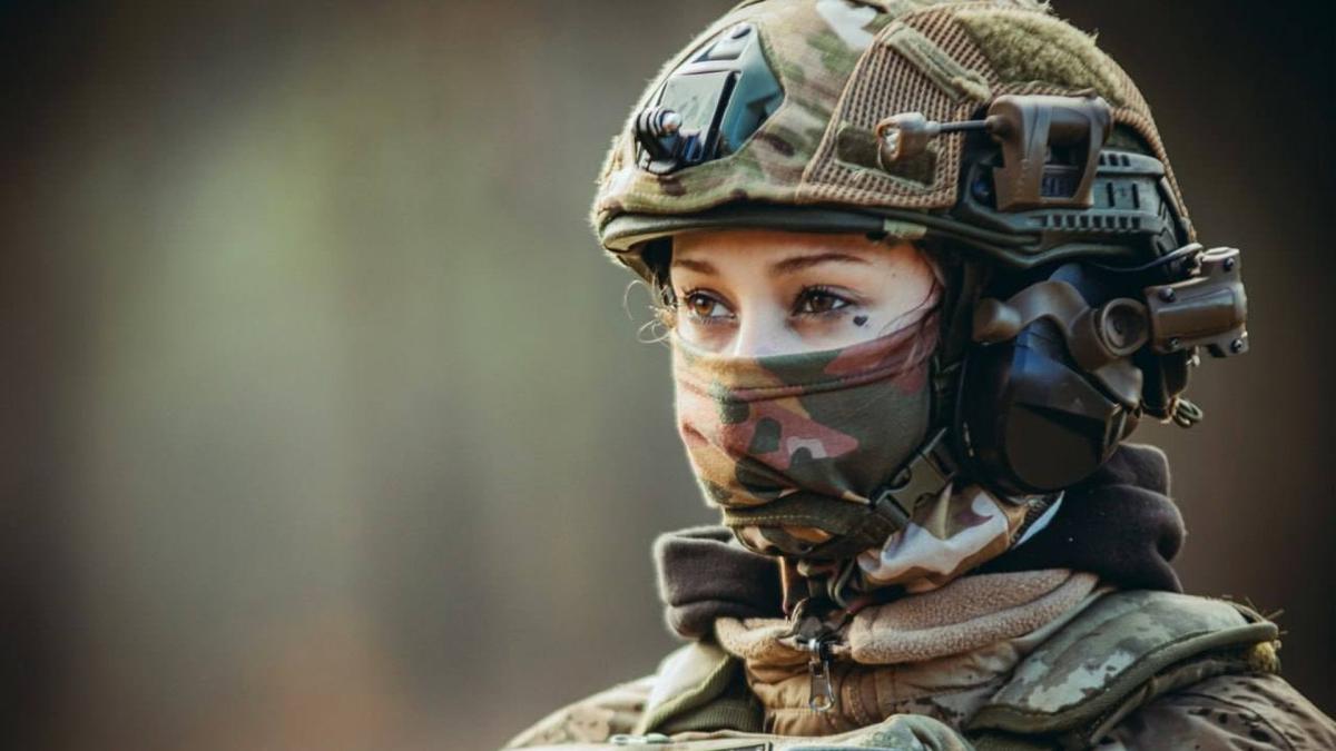 Жінка військова дивиться вдалечінь, її обличчя наполовину закрите балаклавою, вона в касці