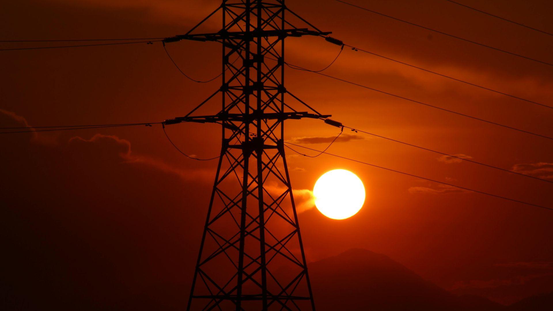 Силова електроопора з лініями електропередач на тлі яскравого заходу сонця