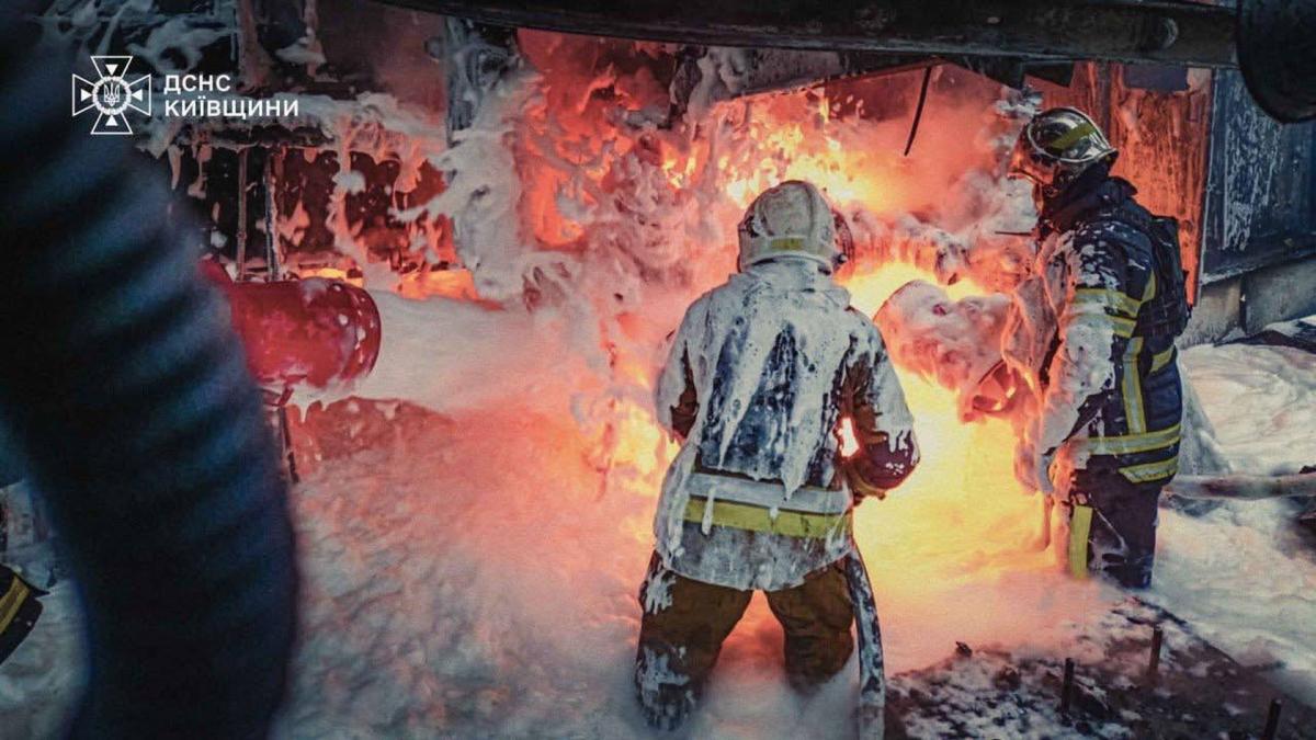 Двоє пожежників у захисних костюмах, вкритих піною, гасять пожежу з відкритим вогнем