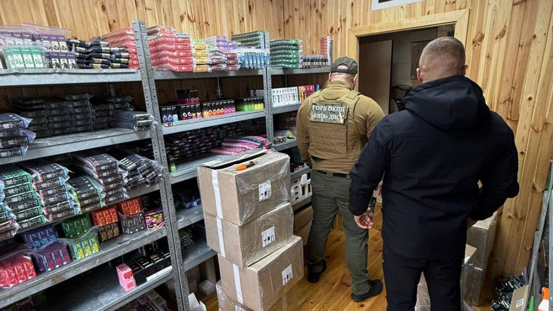 Два правоохоронці стоять біля стелажів із незаконними вейпами