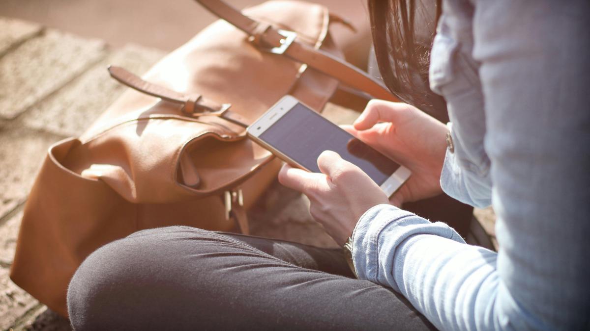 Дівчина сидить на підлозі в позі лотос і тримає у руках мобільний телефон