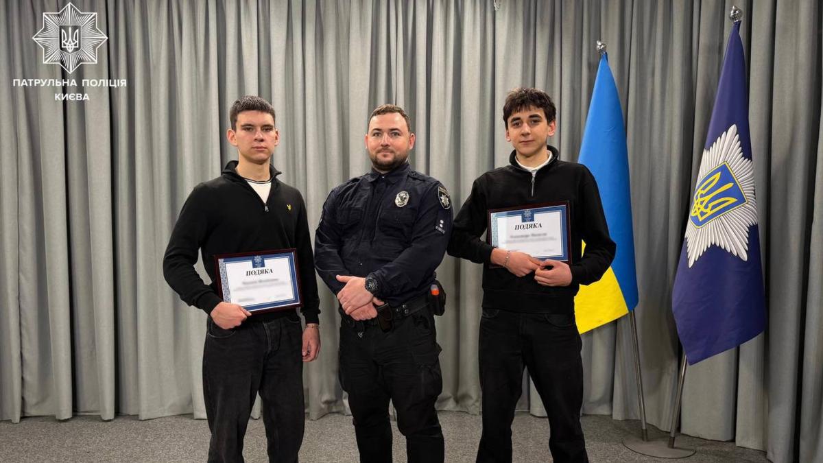 Поліцейський стоїть в оточенні двох школярів, яким вручили грамоти