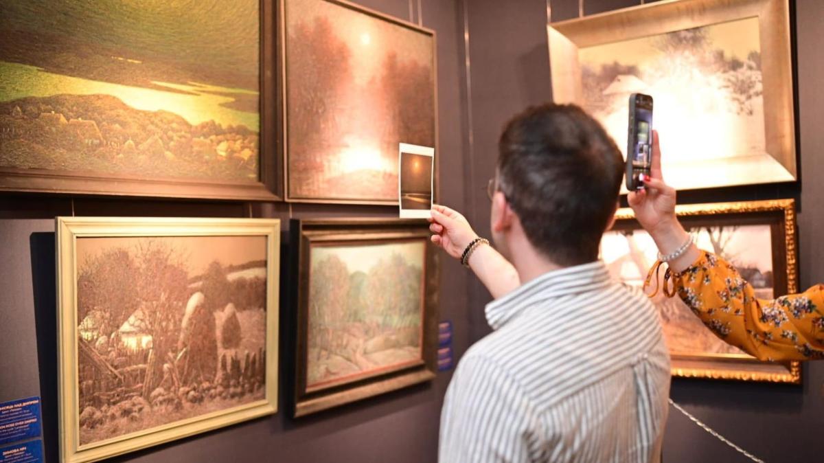 Відвідувачі на виставці розглядають та фотографують картини
