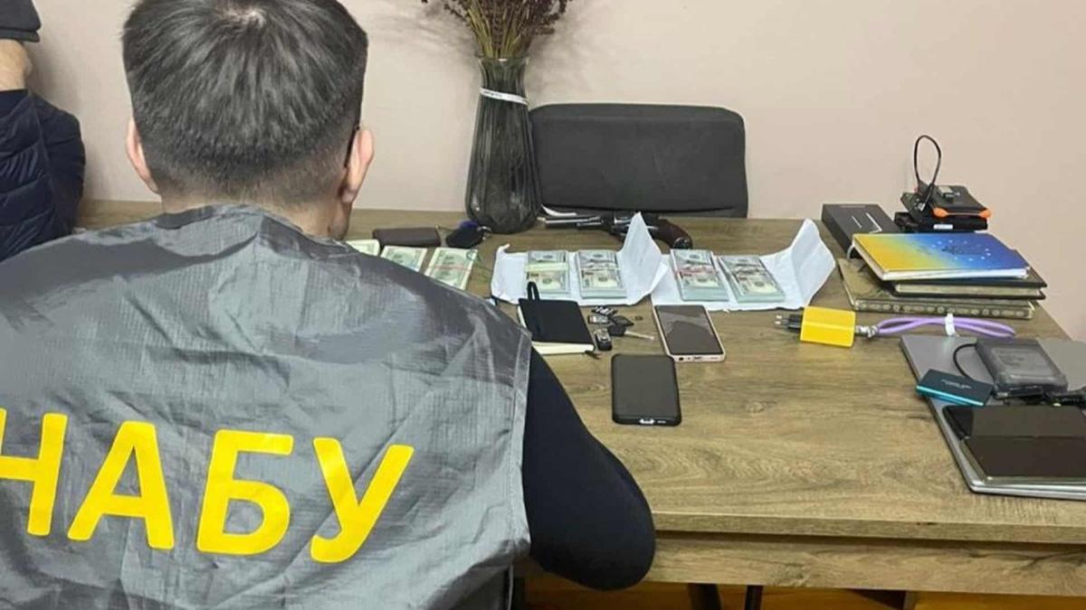 $3,5 млн за закриття справи: затримано прокурора ОГП та адвокатів Працівник НАБУ сидить за столом, на якому розкладені речові докази справи: гроші і документи