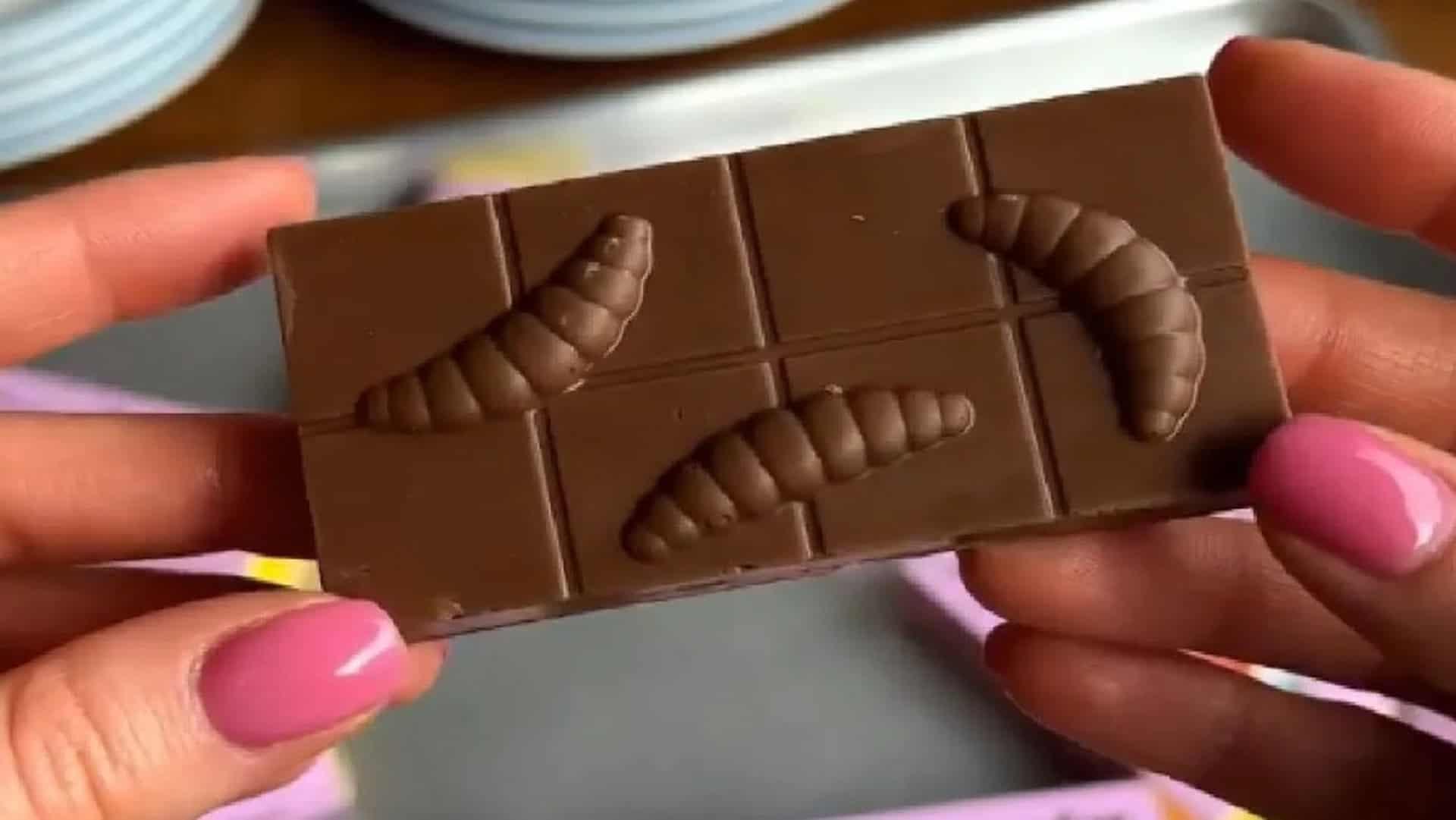 Людина тримає плитку шоколаду, на якій вилиті об’ємні фігурки личинок