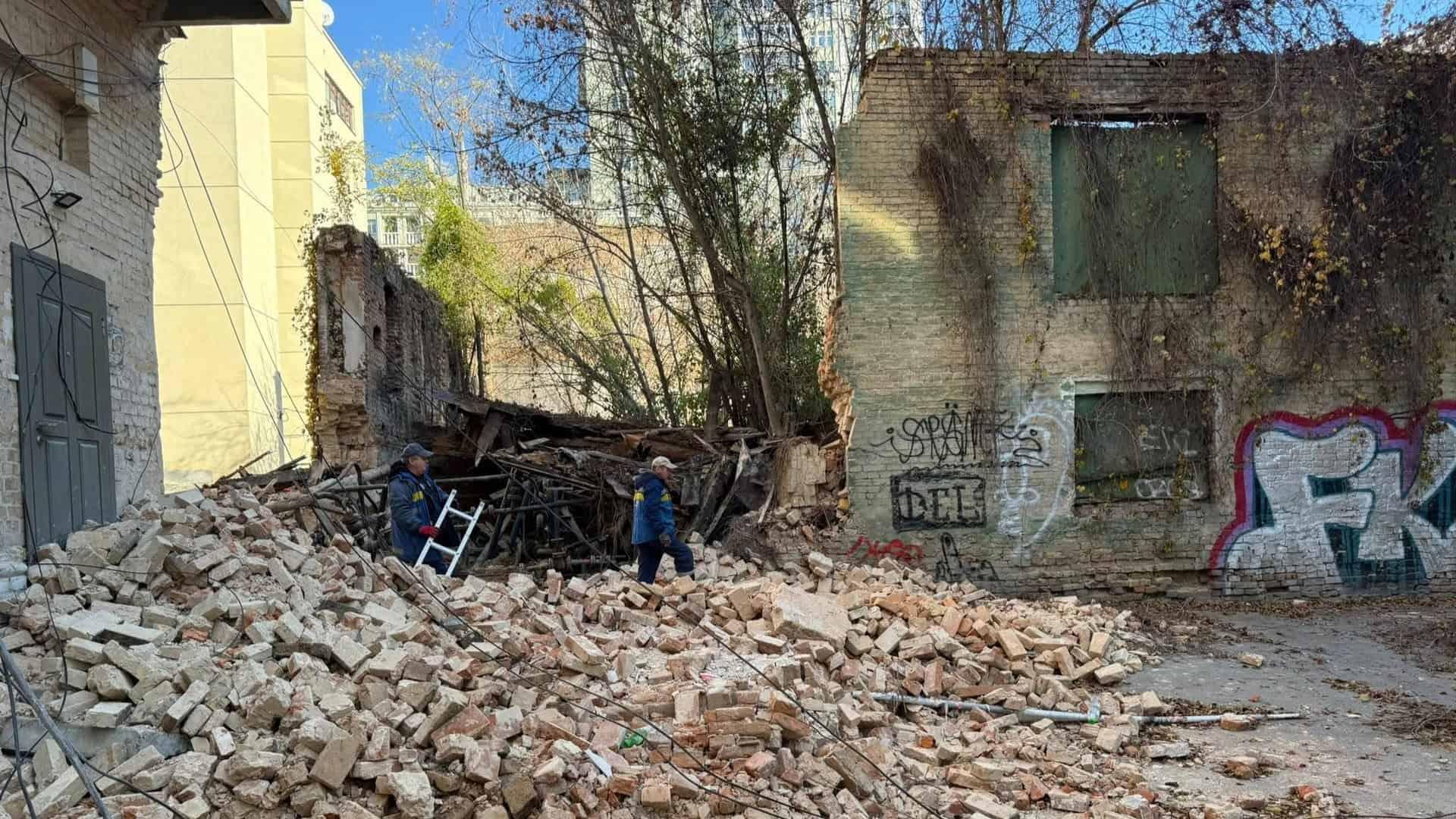 Зруйнована цегляна будівля, купа уламків та двоє людей на руїнах