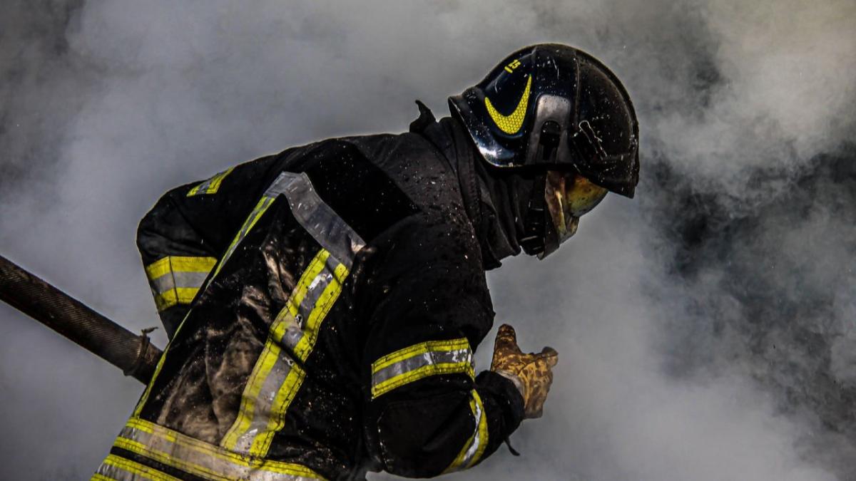 Пожежник у повній амуніції та шоломі працює серед густого диму