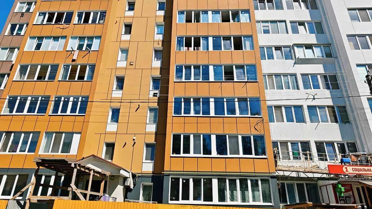 У Бородянці ремонтують дев’ятиповерхівку для 216 мешканців Вигляд сучасної жилої багатоповерхівки в Києві з яскраво оранжевими та білими фасадами, новобудова та ремонтні роботи у дворі, місто активно розвивається.