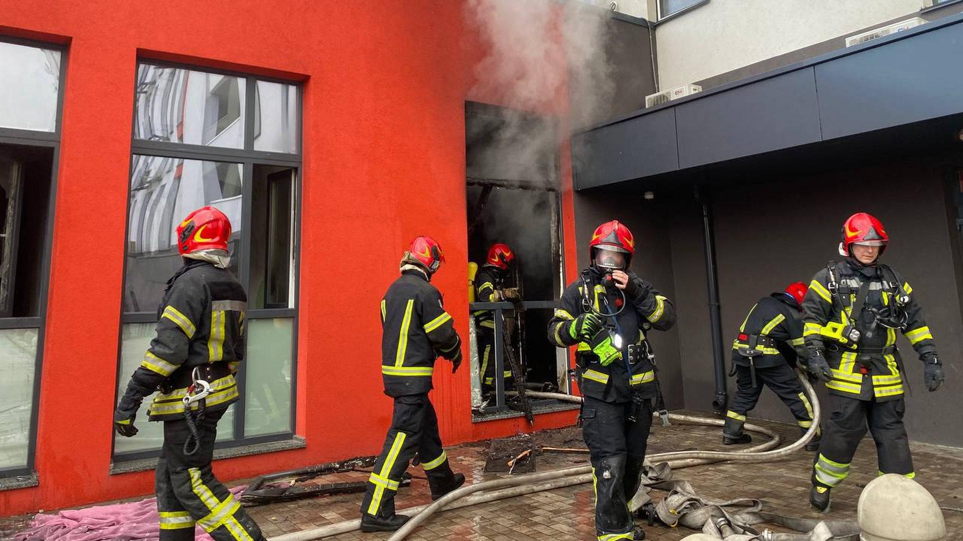 Багато пожежників біля будинку із червоними стінами, рятувальники гасять пожежу