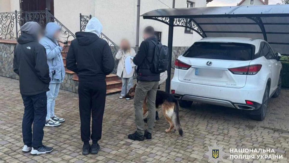 У Києві викрили схему привласнення тютюнових виробів на 128 мільйонів гривень слідчі дії біля приватного будинку: кілька осіб у верхньому одязі стоять поруч із білим автомобілем