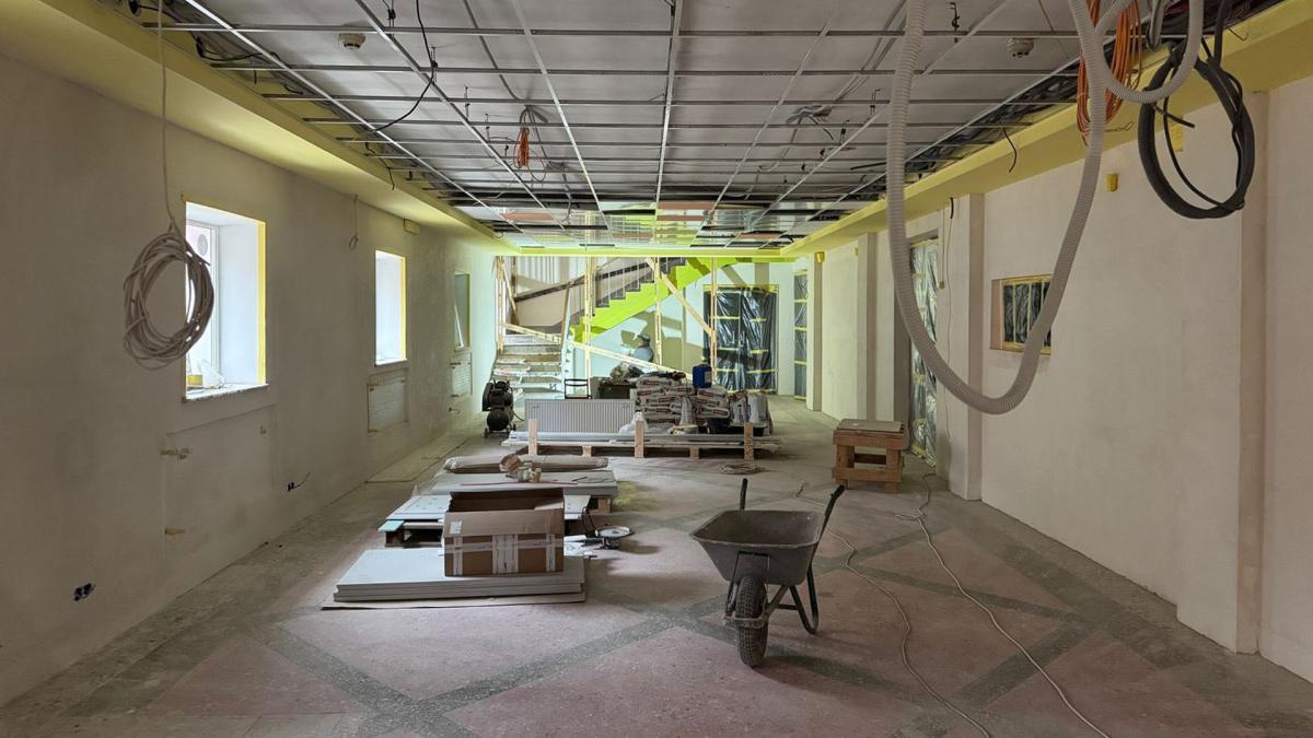 Велике приміщення в процесі ремонту з відкритими стельовими балками, будівельними матеріалами та тачкою