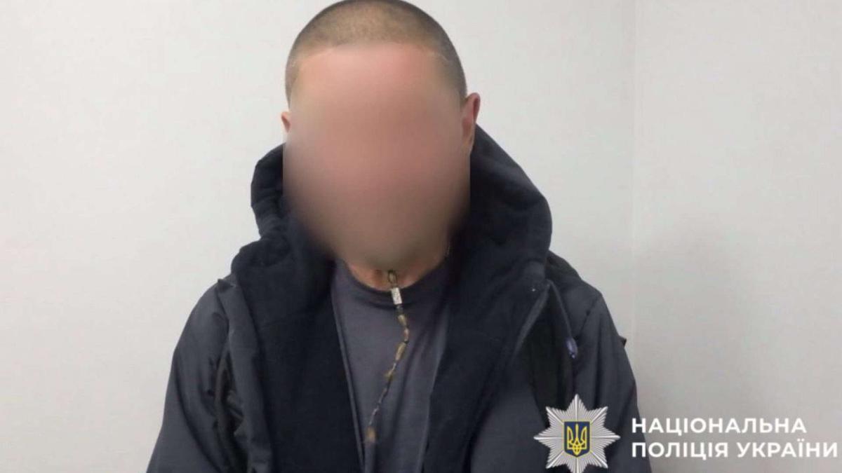 Чоловік в темній куртці сидить на фоні білої стіни із заблюреним обличчям