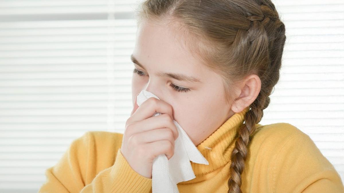 Дівчинка в жовтому светрі витирає ніс серветкою – вона застудилася