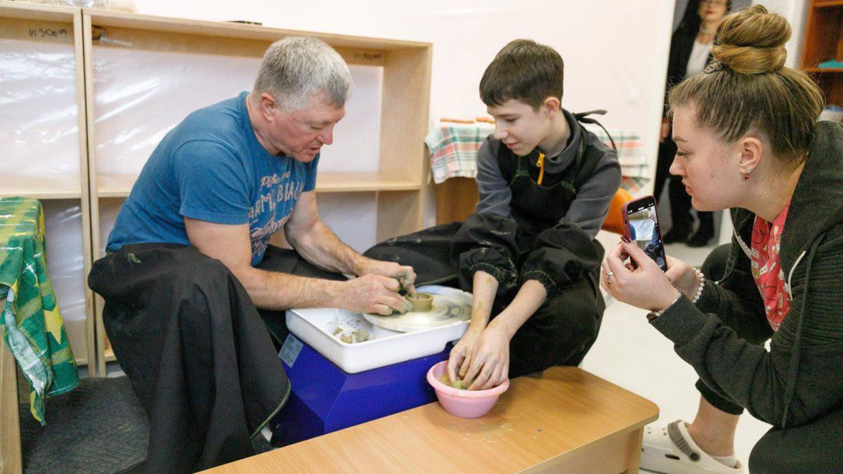 Чоловік-вчитель показує хлопчику як правильно зробити глечик з глини на гончарному колесі