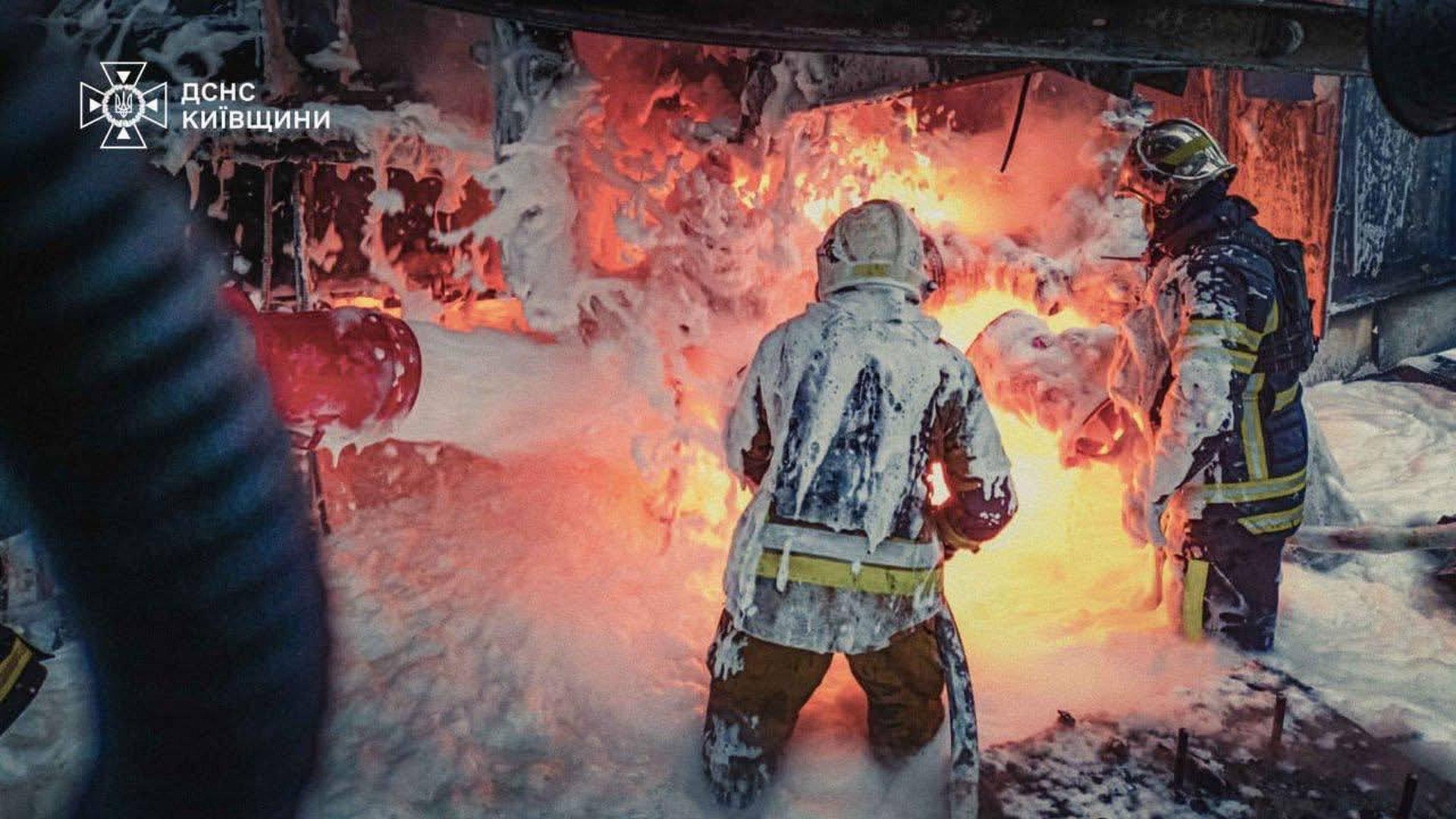 Двоє пожежників у захисних костюмах, вкритих піною, гасять пожежу з відкритим вогнем