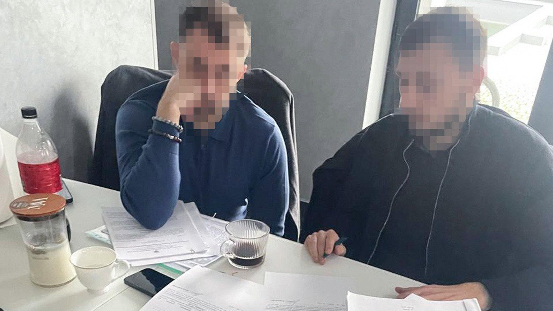 Два чоловіки сидять за столом із заблюреними обличчями
