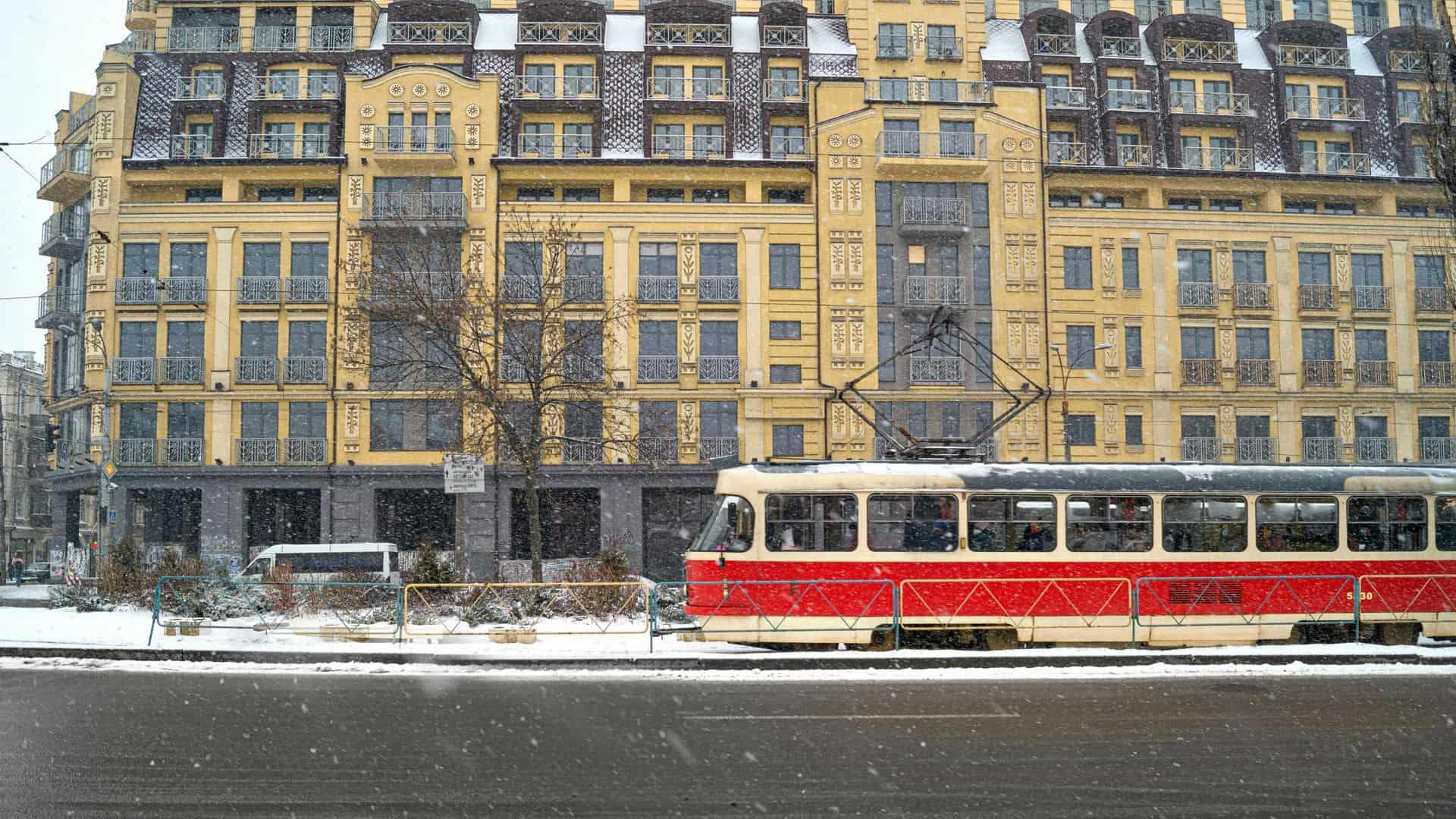 Червоно-жовтий трамвай рухається засніженою вулицею повз жовту будівлю
