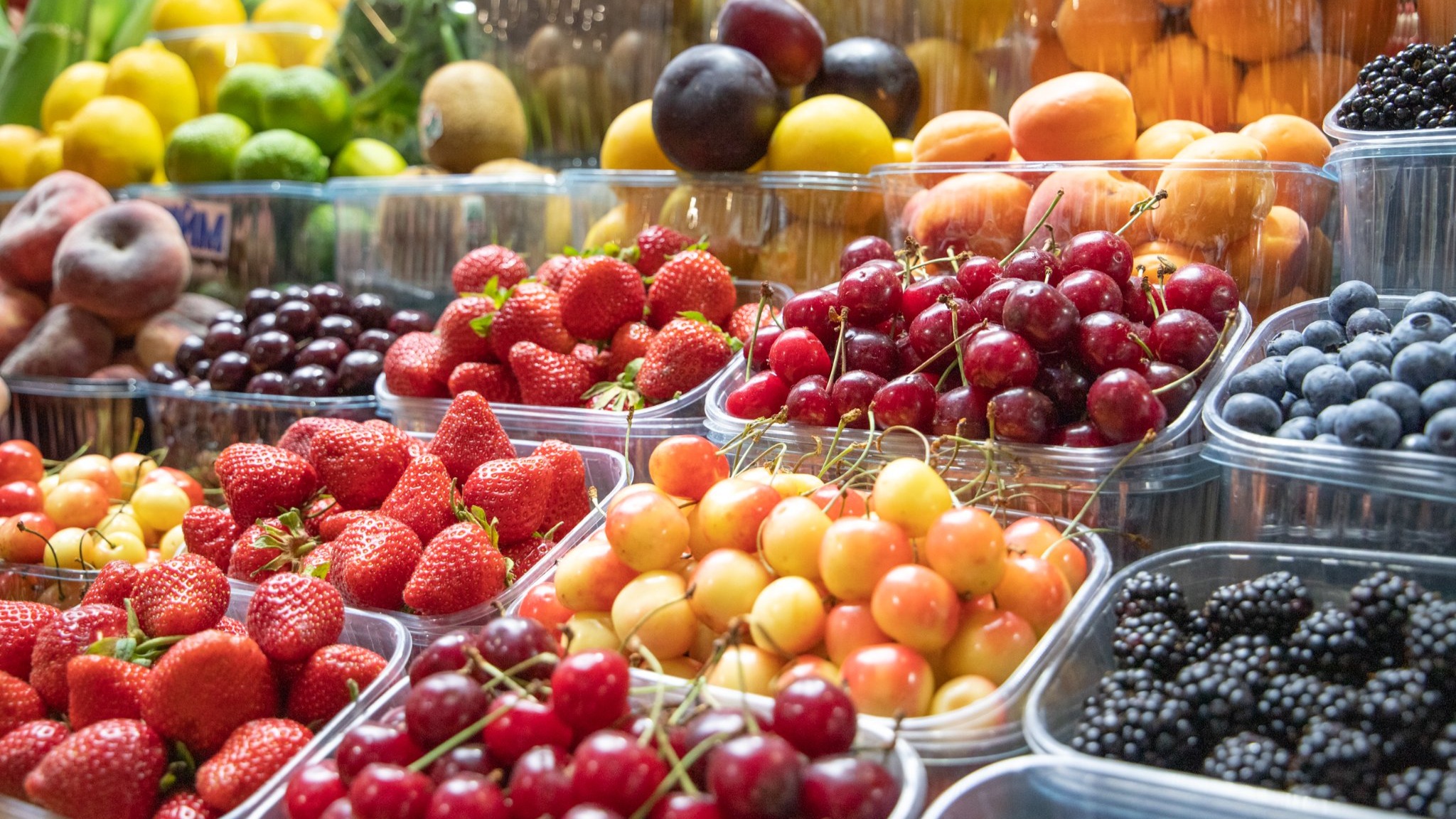 Стіл, вкритий прозорими пластиковими контейнерами з різними ягодами та фруктами
