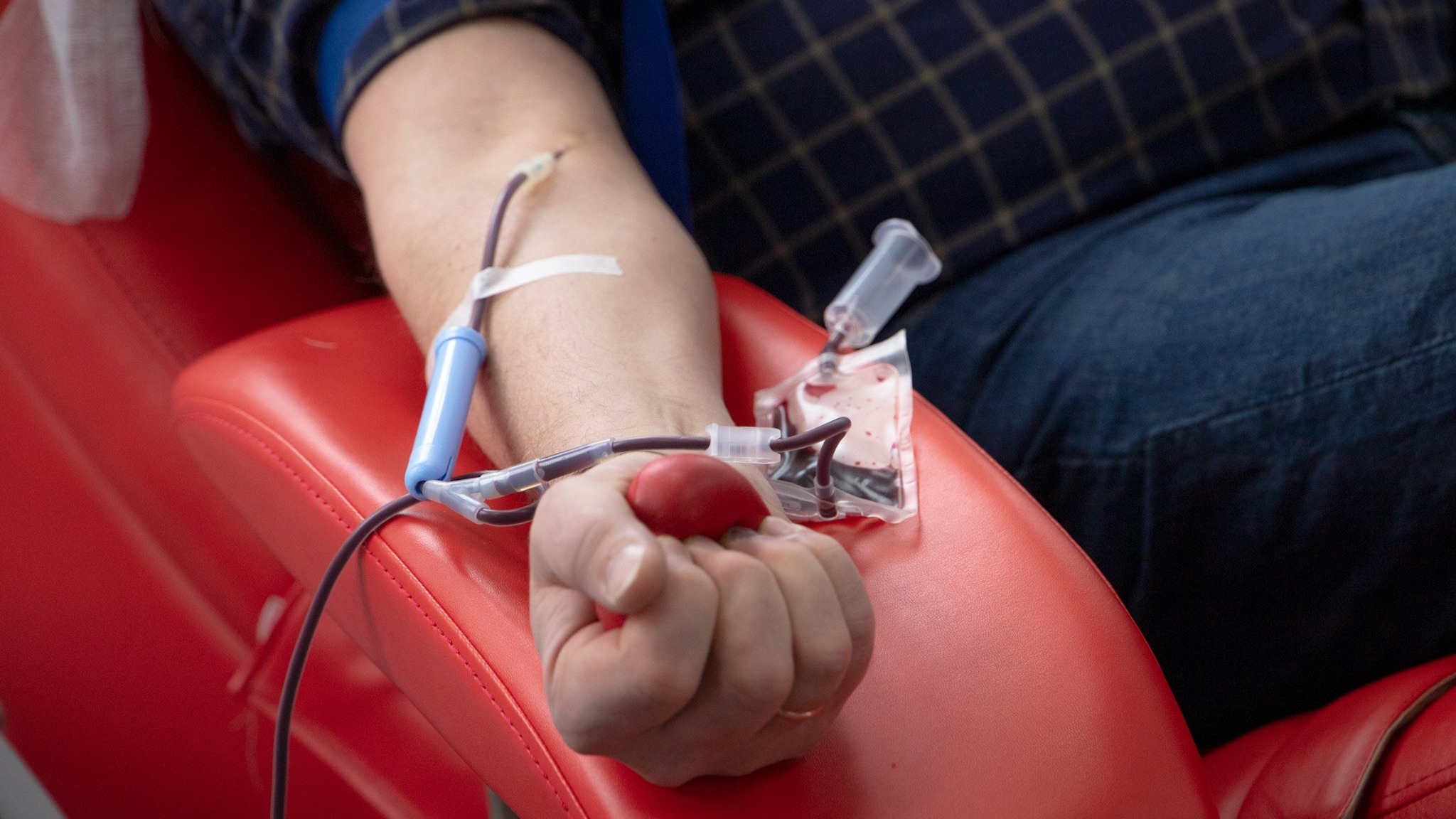 Сидяча людина стискає гумову грушу під час процедури здачі крові