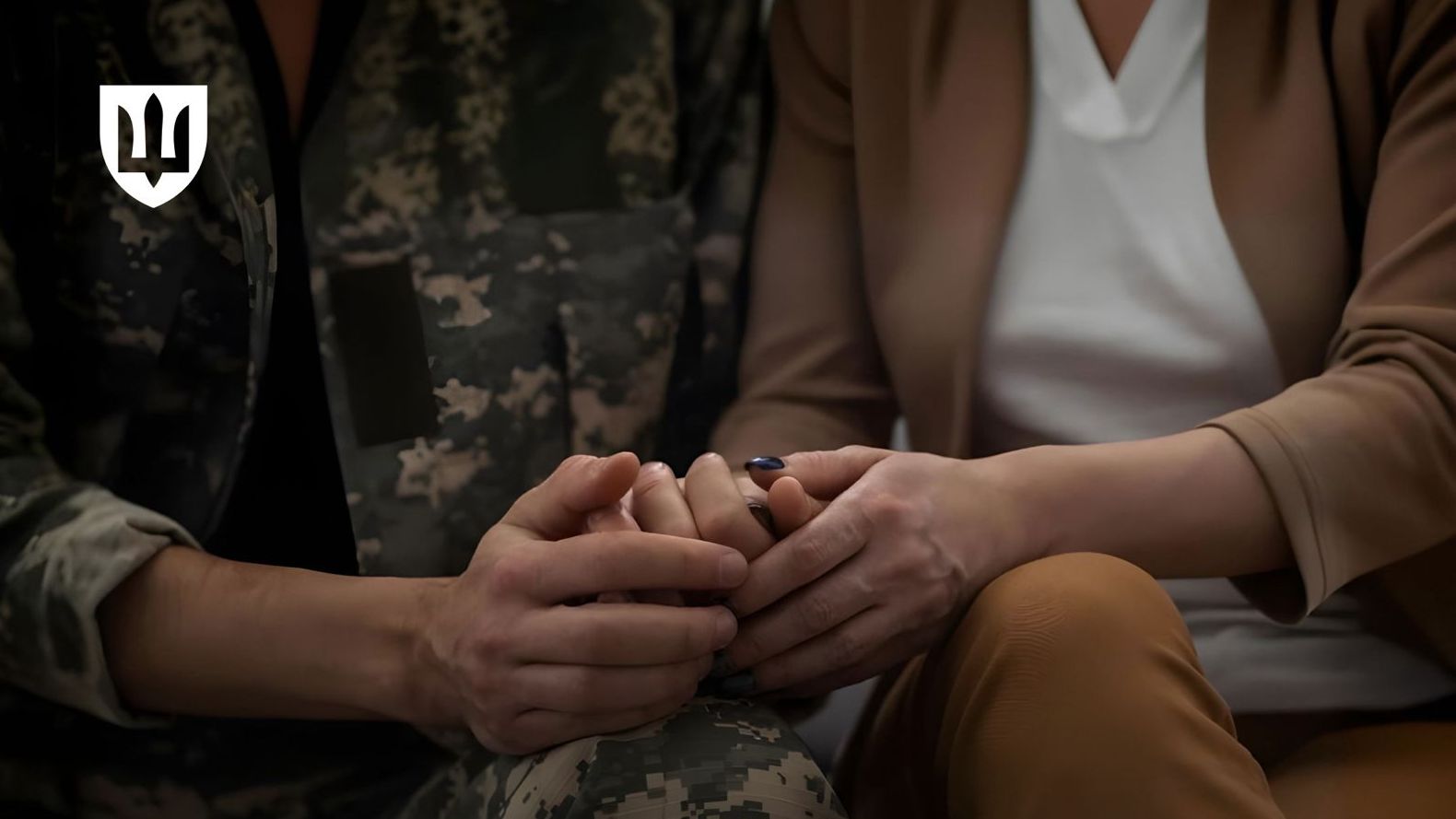 Рука військовослужбовця у піксельній камуфляжній формі ніжно тримає руку жінки в діловому одязі