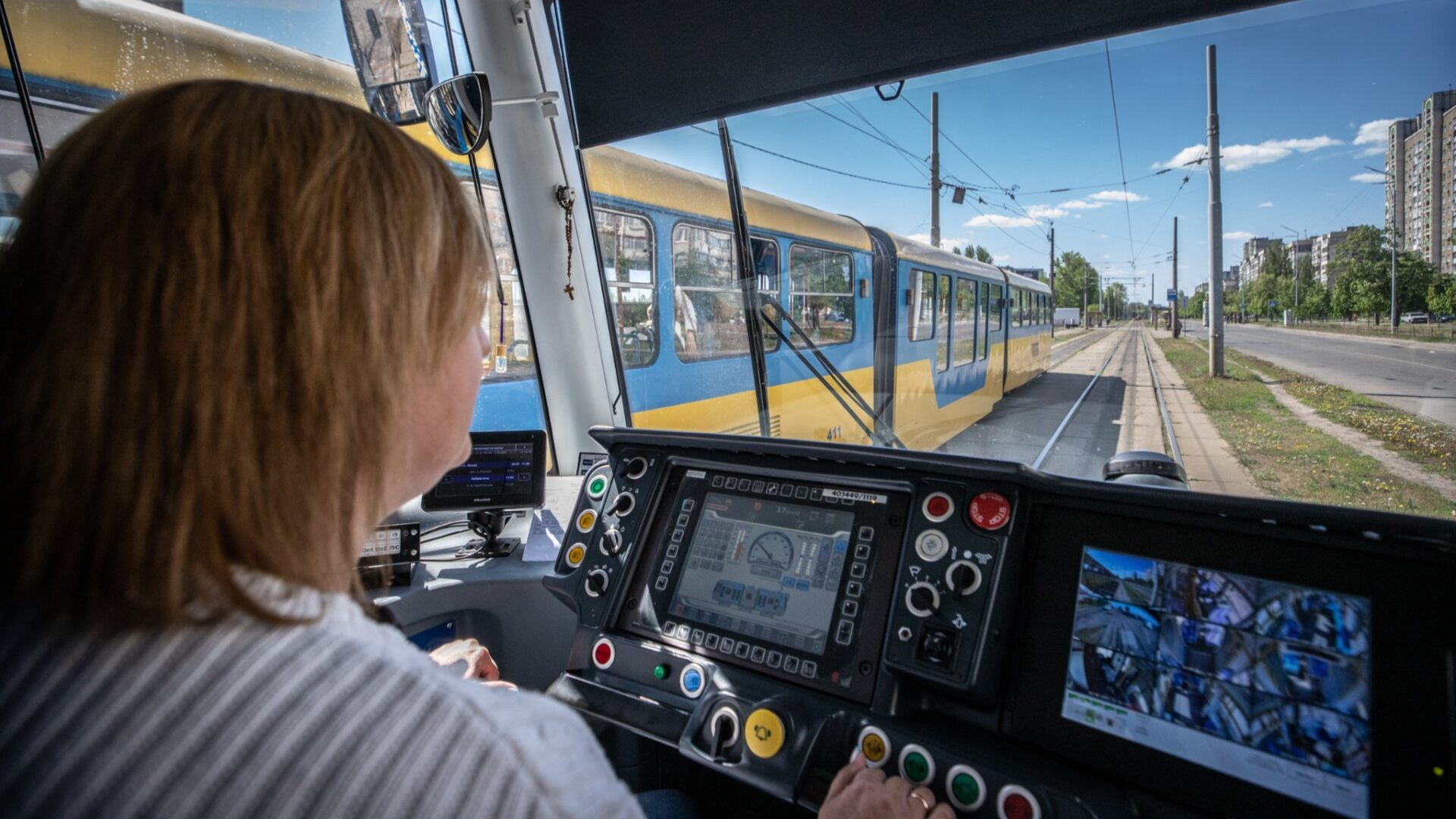 Водійка керує сучасним трамваєм із панеллю управління, де видно екрани з камерами та прилади