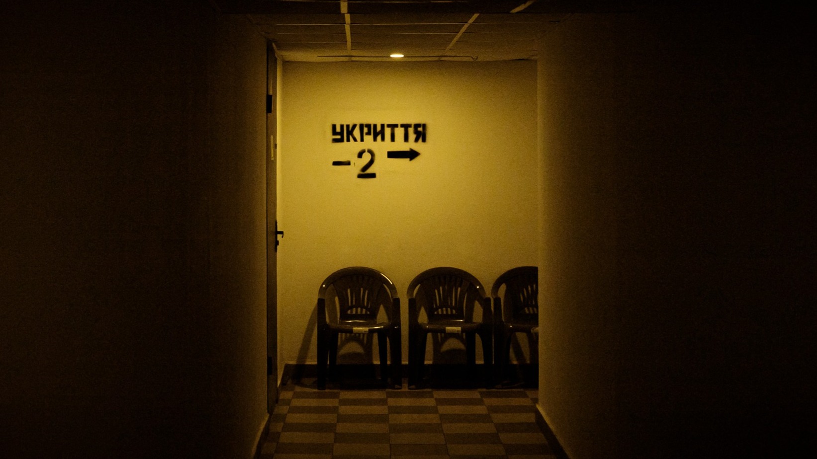 Темний підземний коридор із жовтим освітленням, у кінці якого на стіні напис «Укриття»