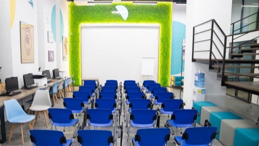 Сучасна лекційна зала з рядами синіх стільців, розташованих перед великою білою стіною-екраном, обрамленою зеленою декоративною панеллю