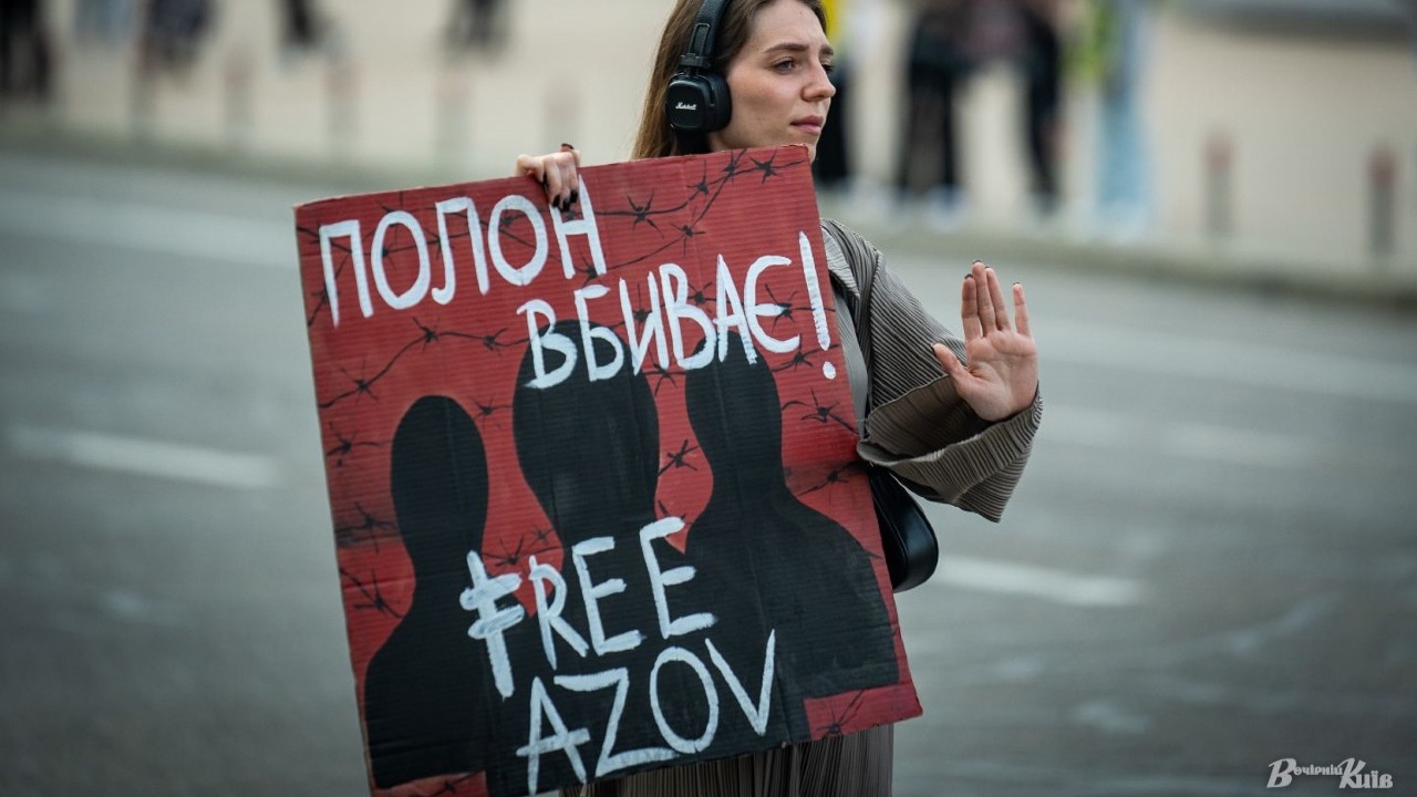 Жінка стоїть на вулиці з плакатом, на якому написано: «Полон вбиває! Free Azov»