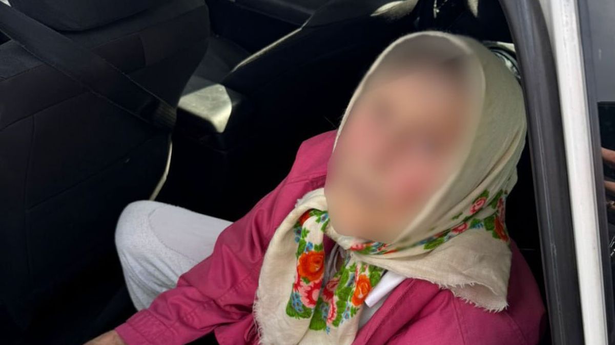 Літня жінка в рожевій куртці та хустці з квітковим орнаментом сидить на задньому сидінні автомобіля, обличчя розмите