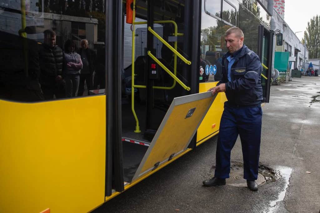 Київ отримав 30 нових автобусів: 20 уже працюють на маршрутах (фото) Працівник у спецодязі перевіряє люк біля дверей нового жовтого автобуса на території автопарку