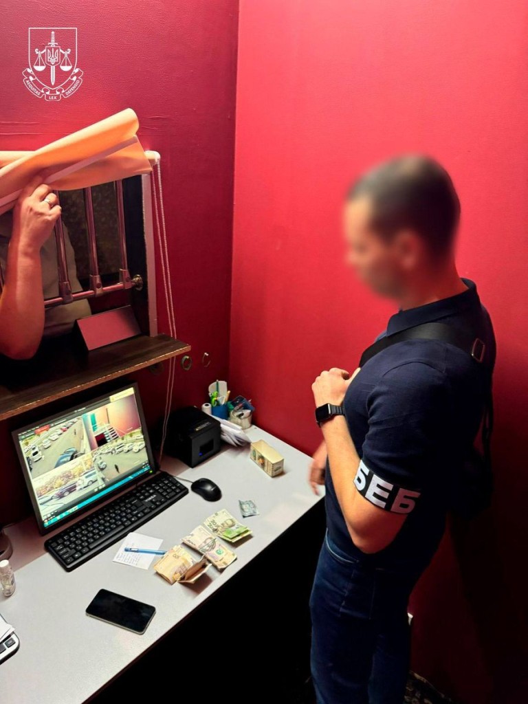 Співробітник «БЕБ» перевіряє касу з грошима у приміщенні з червоними стінами