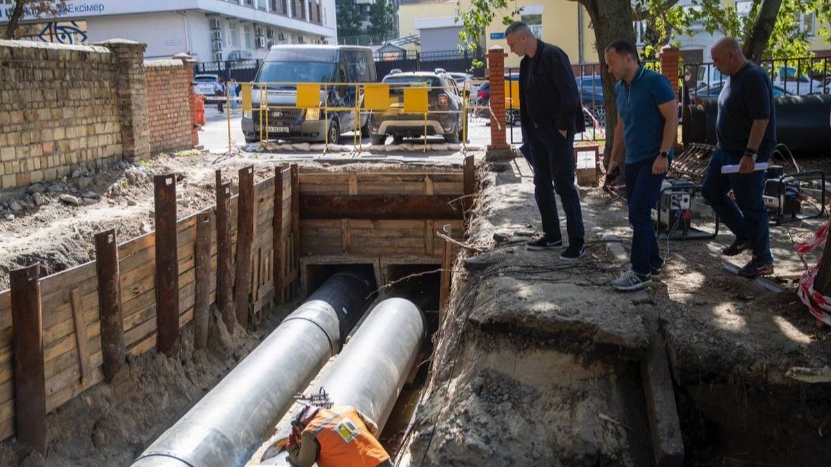 Троє чоловіків оглядають розкопану ділянку з великими трубами під час ремонту тепломережі