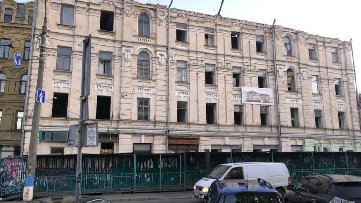 Зруйнована старовинна будівля у центрі Києва з пошкодженими вікнами та фасадом, що потребує ремонту, на тлі міського руху та огорожі безпеки.