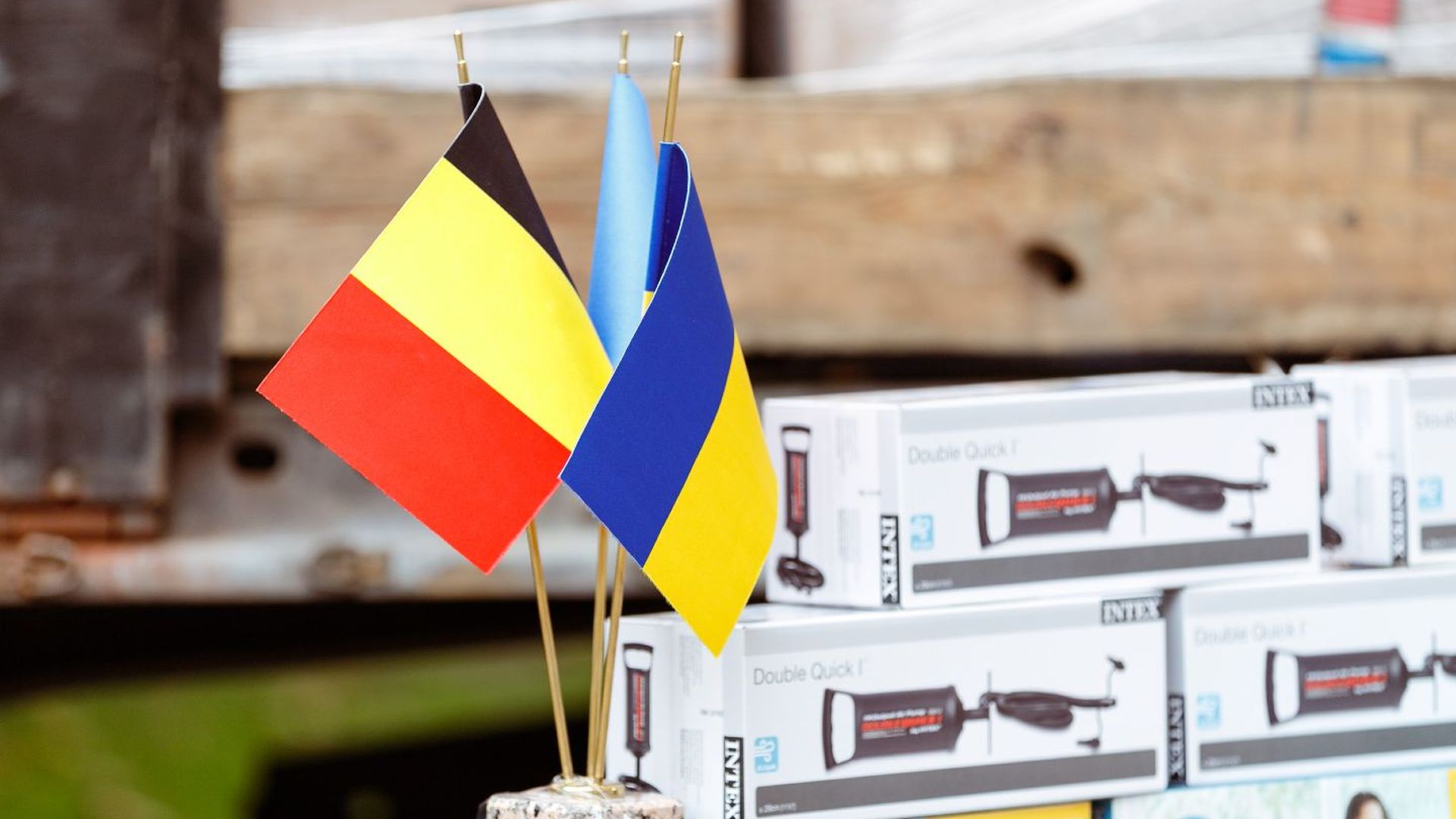 Прапорці Бельгії та України встановлені поруч на підставці на тлі коробок із насосами
