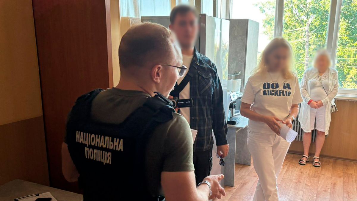 Поліцейський у жилеті з написом «Національна поліція» проводить процесуальні дії в приміщенні, перед ним стоять троє людей із розмитими обличчями