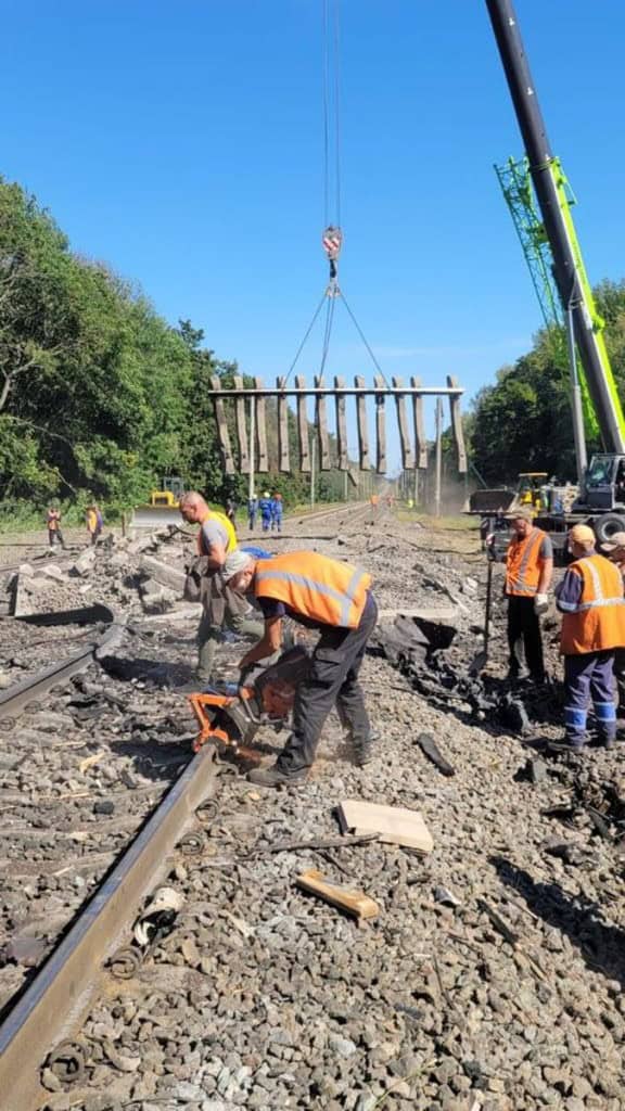 ДСНС і Укрзалізниця показали, як відновлюють рух після вибухів під Києвом (фото) Робітники ремонтують залізничні колії, один ремонтує рейку, кран підіймає великі шпали