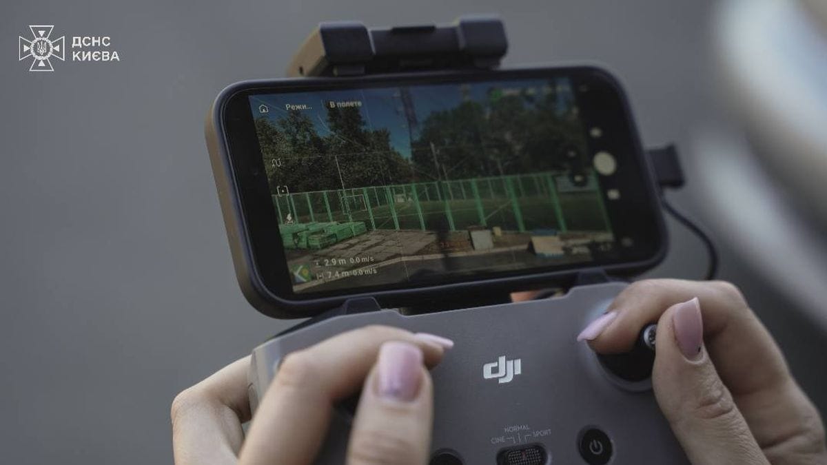 Квадрокоптер або дрон управляється через смартфон з дисплеєм на задньому фоні, демонструючи план польоту та навігаційні дані.