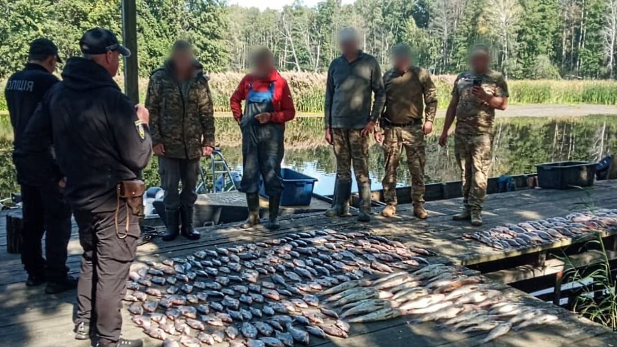 Група чоловіків у камуфляжі та поліцейські стоять на дерев’яному помості біля водойми, перед ними на підлозі викладено велику кількість виловленої риби